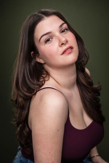 Young woman with long brown hair posing against a dark background.