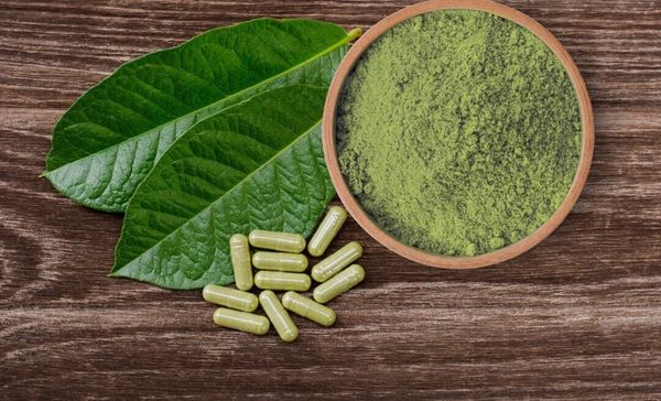 Green herbal powder, capsules, and leaves on wood.