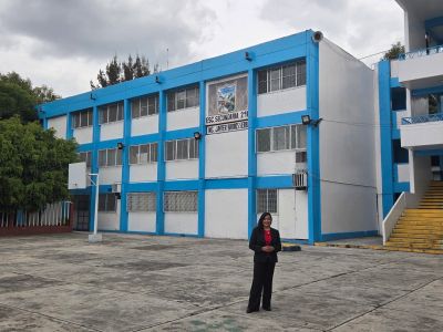 Edificio escolar azul con mujer de pie.
