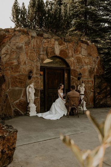 Bride and groom seated outside stone building.