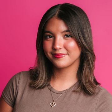 Young woman with straight brown hair smiling against a pink background.