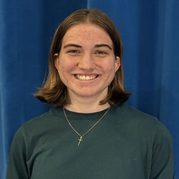Young person smiling in front of a blue curtain.