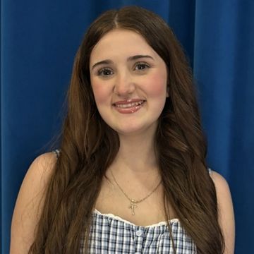 Young woman smiling with long hair against a blue curtain background.