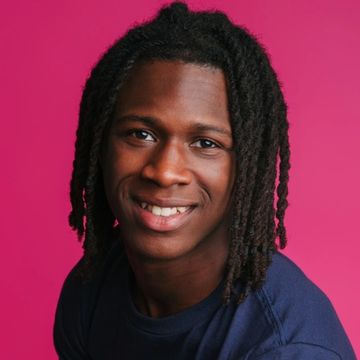 Young man with dreadlocks smiling against a bright pink background.