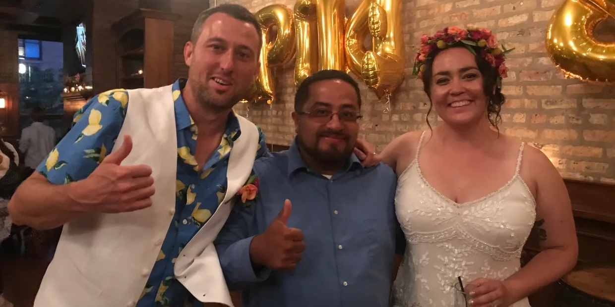 Three people smiling and posing indoors, two giving thumbs up.