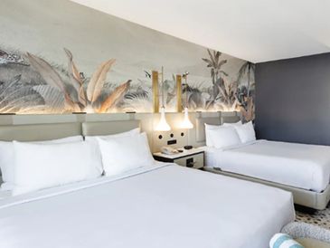 Modern hotel room with two queen beds and artistic wall decor.