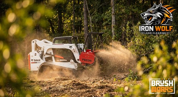 A Bobcat machine clearing land in a forest with Iron Wolf and Brush Works logos.
