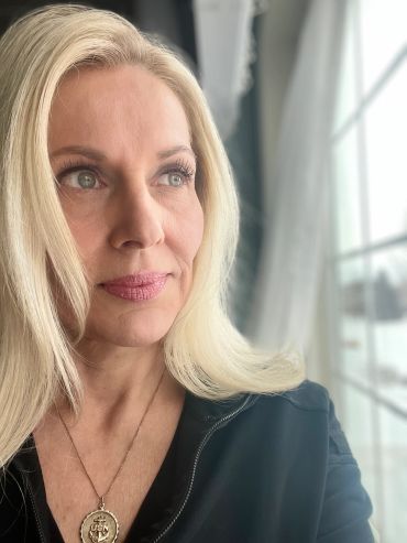 Blonde woman gazing thoughtfully out a window.