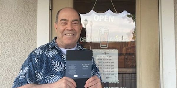 Smiling man holding a book outside a cafe door.