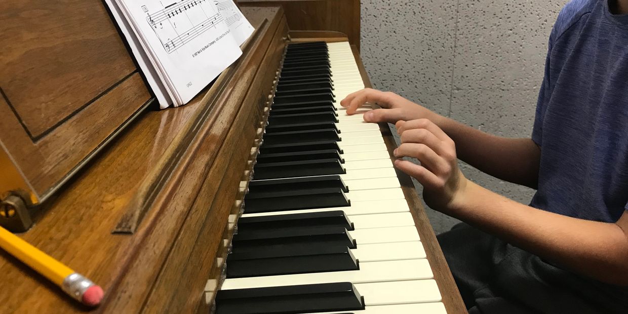Close-up of a child's hands playing an upright piano with music and a pencil sitting on the piano.  
