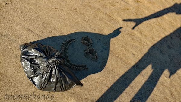 Shadow art on sand using a bag and a person's shadow.