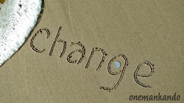 The word 'change' written in the sand near ocean waves.