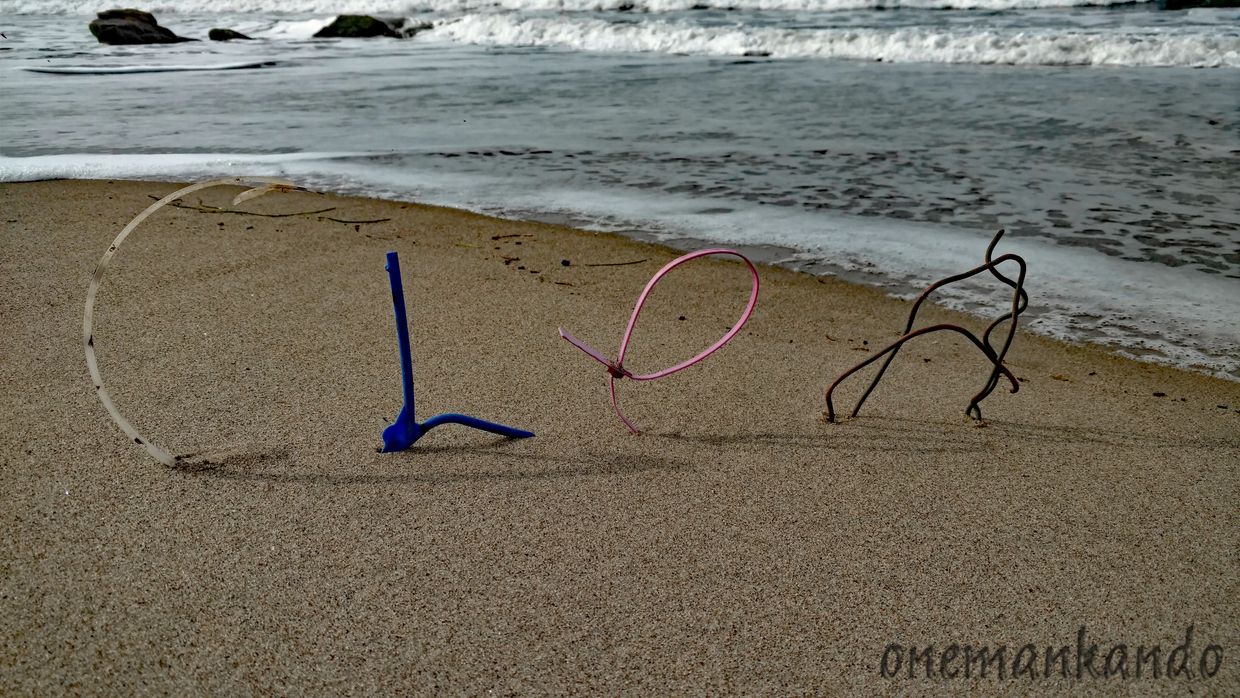 Letters made of bent plastic and wire on a sandy beach near the ocean.