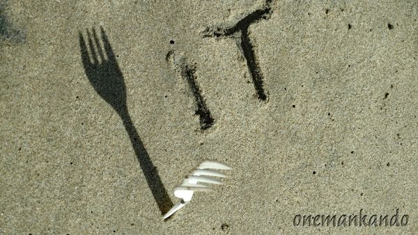 A shadow of a fork on sand forming the word 'IT'.