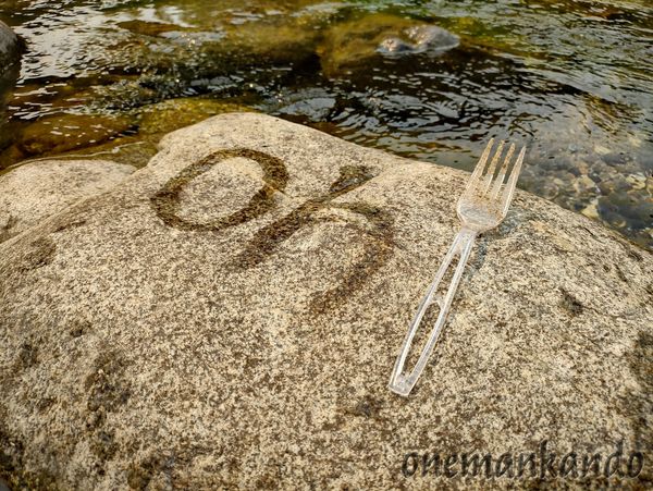 The word 'ok' written with water on a rock beside a plastic fork.