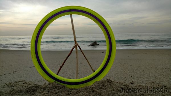 A peace symbol made of sticks inside a circular ring on a beach at sunset.