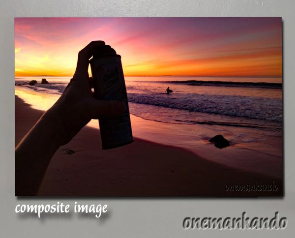 Hand holding a can against a vibrant sunset beach scene with a surfer in the water.