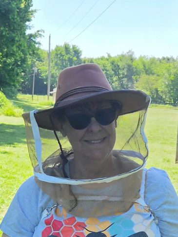 Woman outdoors wearing a protective bee-keeping hat and sunglasses.