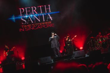 Perth Santa performing live with band in Singapore, vibrant red stage lights.