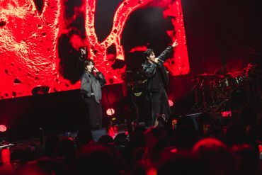 Two performers on stage with a vibrant red background during a concert.