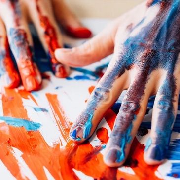 Hands covered in blue and red paint creating artwork.