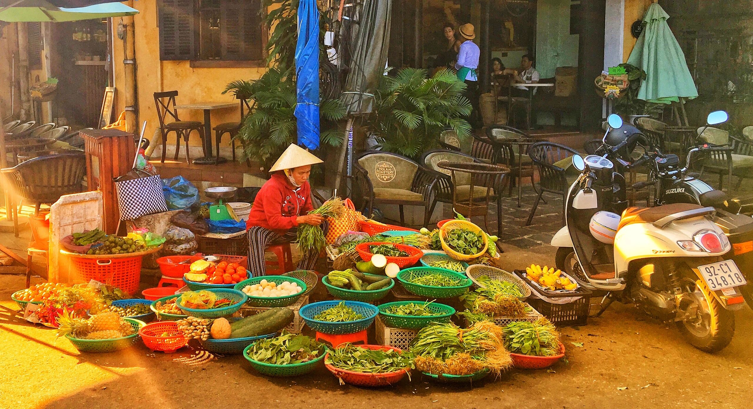 Mujer con sombrero tradicional vendiendo verduras frescas en la calle.