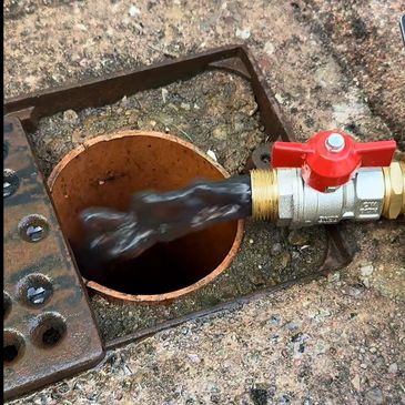 A valve releases dark liquid into a drain on a concrete surface.