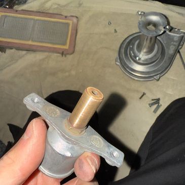 Hand holding a mechanical part with screws and another component in the background.