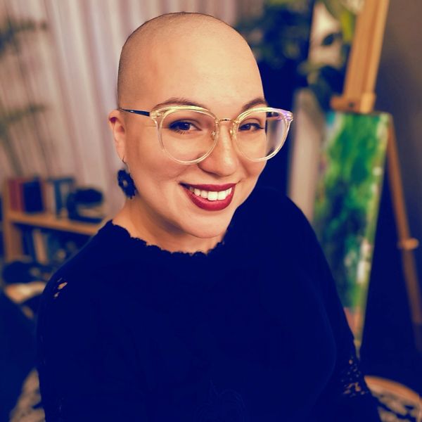 A woman with glasses and bald head smiling.