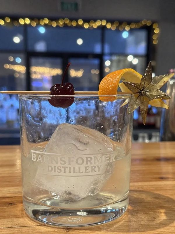 Cocktail in a glass with ice, cherry, orange peel, and star garnish.