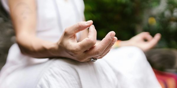 Person meditating with hands in a mudra gesture, wearing white clothing.