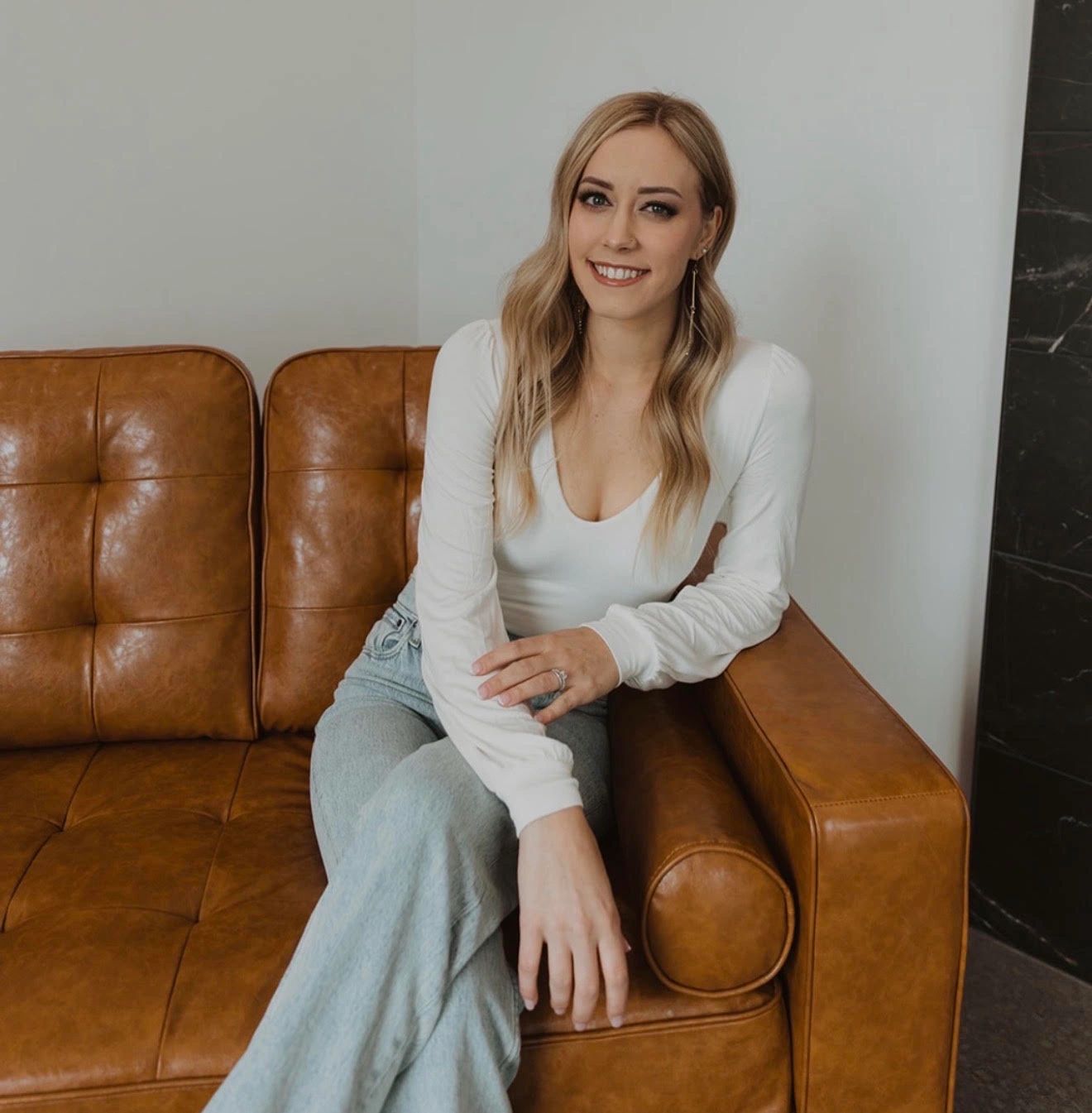 Woman smiling on a brown leather couch.