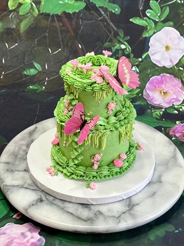 Green two-tier cake decorated with pink butterflies and flowers.
