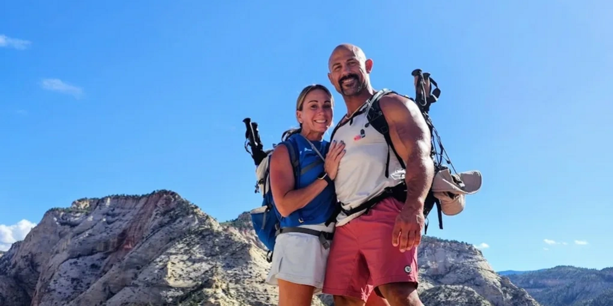 A happy couple hiking with backpacks in a mountainous area under a clear blue sky.