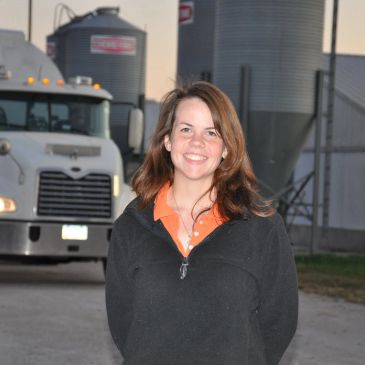 Woman smiling in front of a truck and silos.