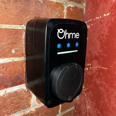 Ohme electric vehicle charger mounted on a brick wall.