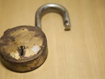 Rusty old padlock unlocked on wooden surface.