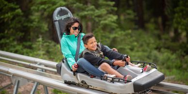 Two people enjoying a ride on a toboggan coaster in a forested area.