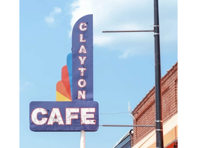 Retro neon sign for Clayton Cafe against a clear blue sky.