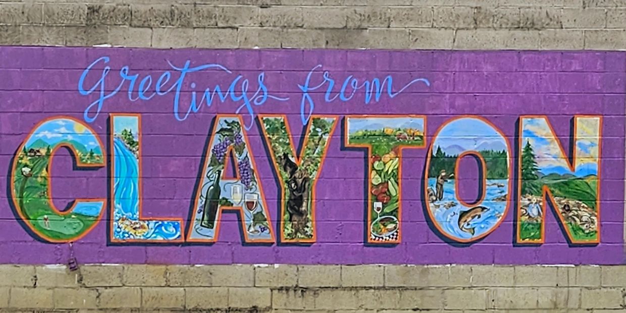 Colorful mural on a brick wall saying 'Greetings from Clayton' with nature and local life scenes inside the letters.
