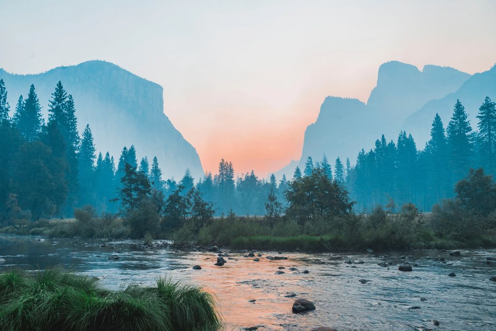 Sunrise over a river with mountains and trees.