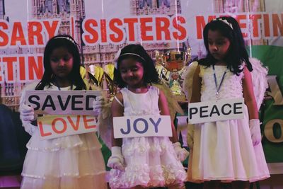 Three young girls in white dresses holding signs with positive words: Saved, Joy, Peace.