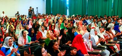 A large audience attentively watching an event, with many women wearing headscarves.