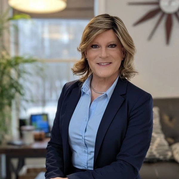 Professional woman in a navy blazer and light blue shirt smiling indoors.