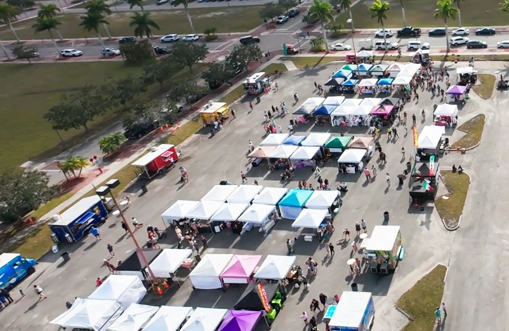 A vibrant outdoor market with colorful tents and food trucks in a sunny parking lot.