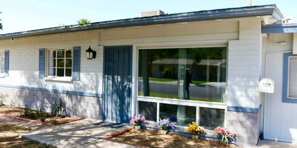 Single-story house with blue door and window shutters, decorated with flower pots.