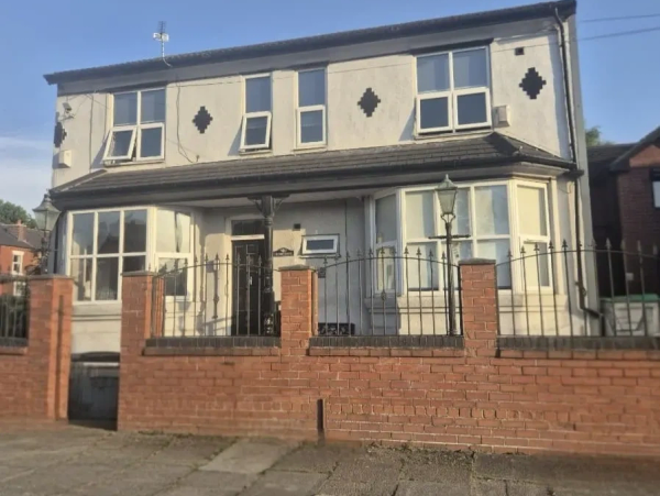 A Victorian property frontage, painted cream, bordered with a low red brick wall topped with iron ra