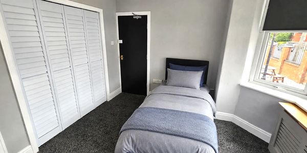 A bedroom at Merrymeet, with a fluffy grey carpet, cool grey, white and neutral tones. A single bed.