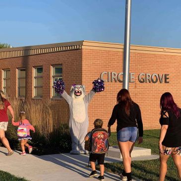 A mascot greets children outside Circle Grove school.