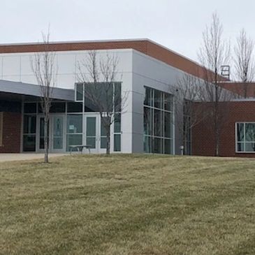 Modern building with glass windows and leafless trees on a grassy lawn.
